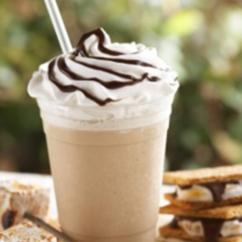 A chocolate milkshake with whipped cream and chocolate drizzle, next to s'mores.