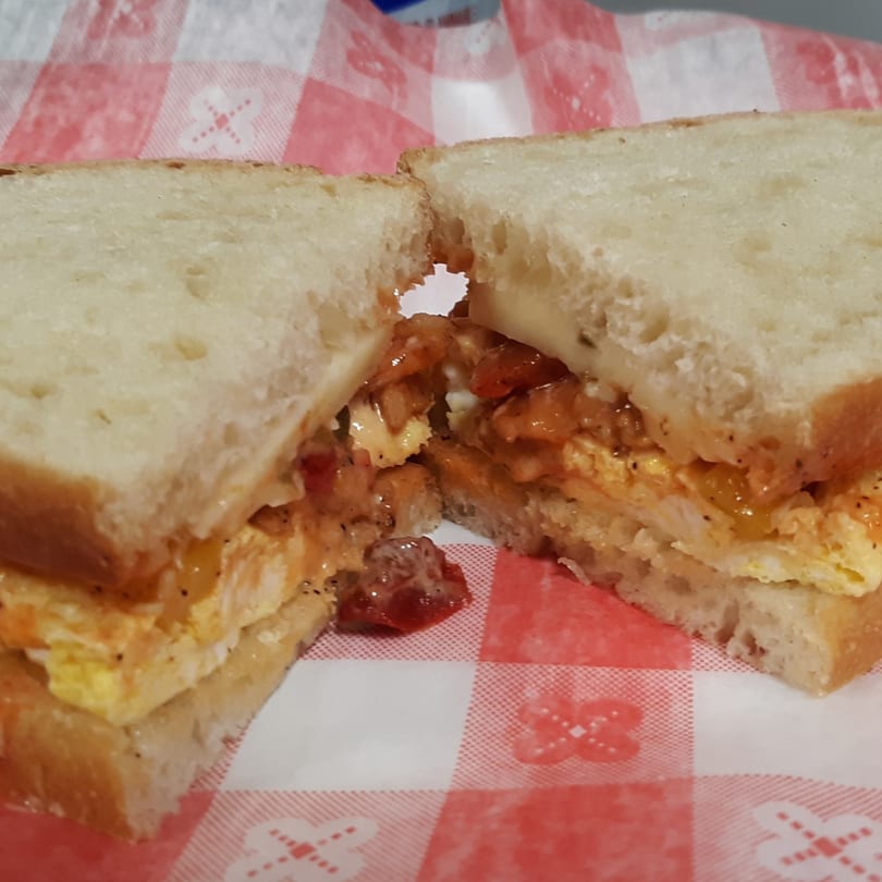A breakfast sandwich with scrambled eggs, cheese, and salsa on white bread, cut in half.