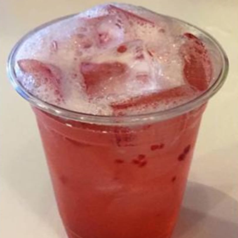 A vibrant red drink with ice and white foam in a clear plastic cup.