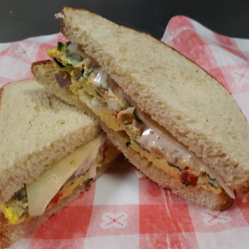Two halves of a sandwich with egg, cheese, and vegetables on white bread, on a red and white checkered napkin.